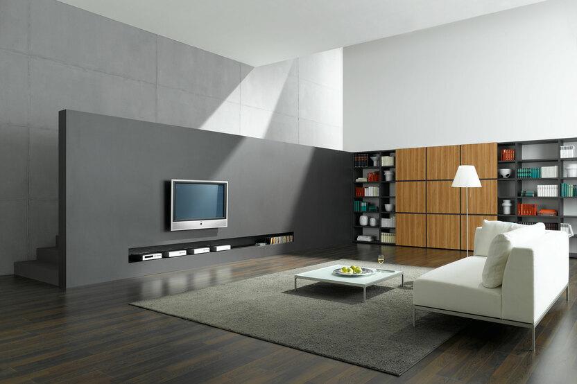 Offene Wohnraumimpression mit grauer TV-Trennwand zur Treppe und Einbauregal aus Holz und weißem Sofa